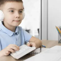 Chłopiec w słuchawkach z kalkulatorem i laptopem przy biurku.