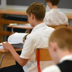 Uczeń w białej koszuli przegląda książkę przy ławce w klasie.