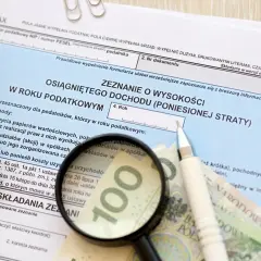 Formularz PIT-38, kalkulator, lupa, długopis i banknot 100 zł.