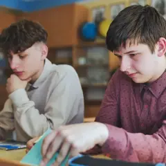 Uczniowie siedzą przy ławkach w klasie, jeden z nich przegląda notatki.