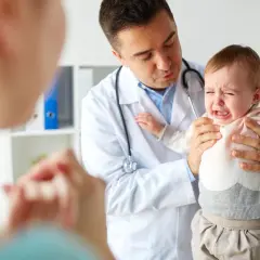 Lekarz trzyma płaczące dziecko, obok stoi matka.