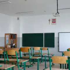 Pusta klasa szkolna z rzędami ławek, tablicą i projektorem.