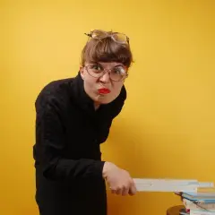 Kobieta w okularach i czarnej bluzce trzyma linijkę nad stosem książek.