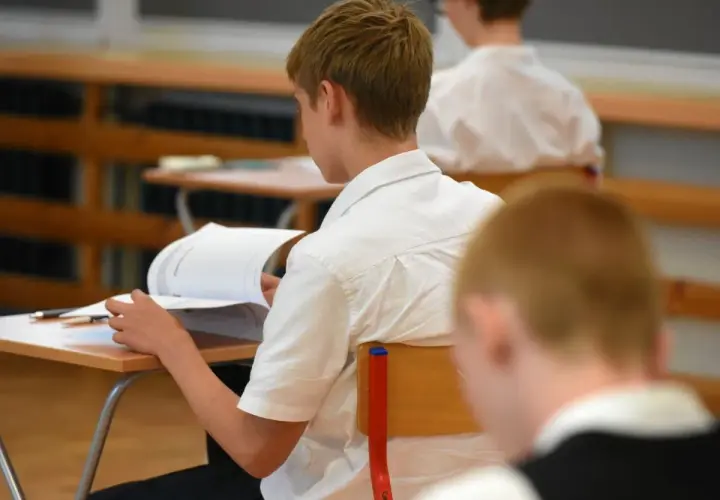Uczeń w białej koszuli przegląda książkę przy ławce w klasie.