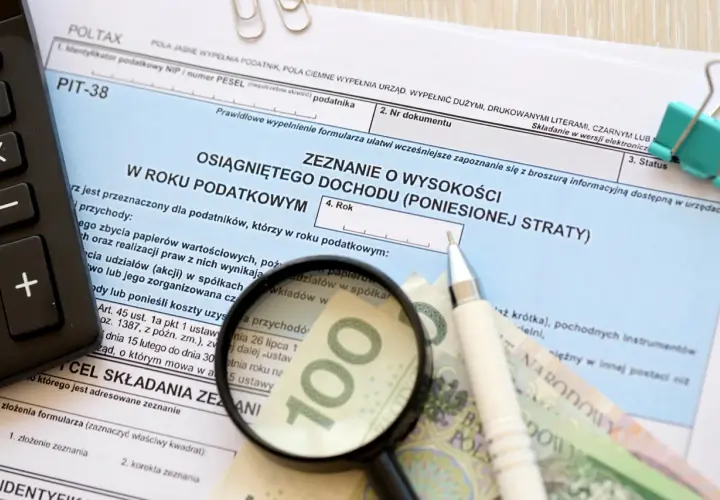 Formularz PIT-38, kalkulator, lupa, długopis i banknot 100 zł.