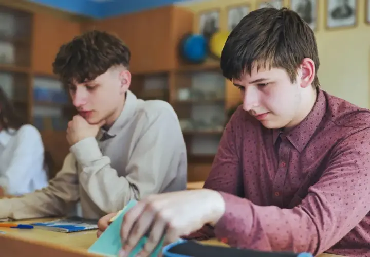 Uczniowie siedzą przy ławkach w klasie, jeden z nich przegląda notatki.