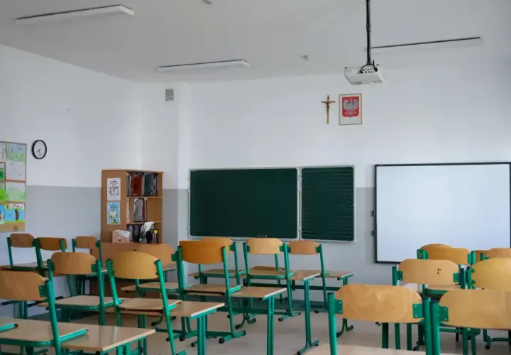 Pusta klasa szkolna z rzędami ławek, tablicą i projektorem.