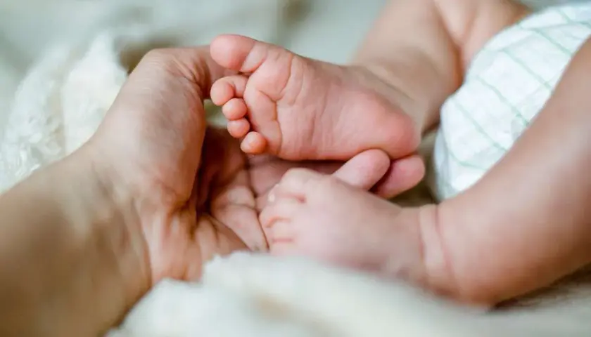 Dłoń dorosłego obejmuje stópkę niemowlaka na miękkim tle.