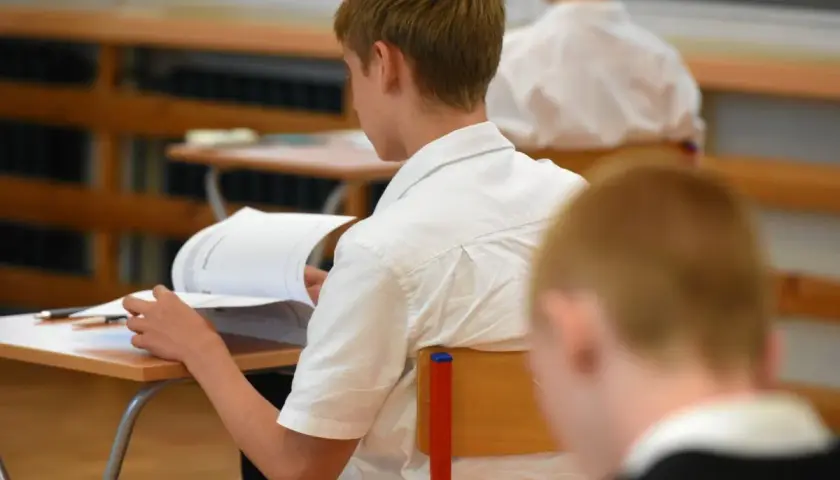 Uczeń w białej koszuli przegląda książkę przy ławce w klasie.