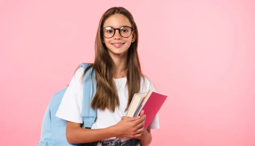 Uśmiechnięta uczennica w okularach z plecakiem i książkami na różowym tle.