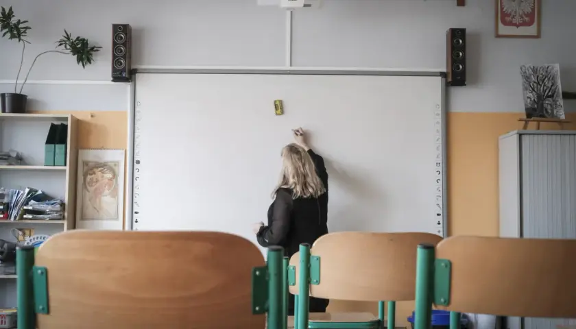 Nauczycielka pisze na tablicy interaktywnej w sali lekcyjnej.