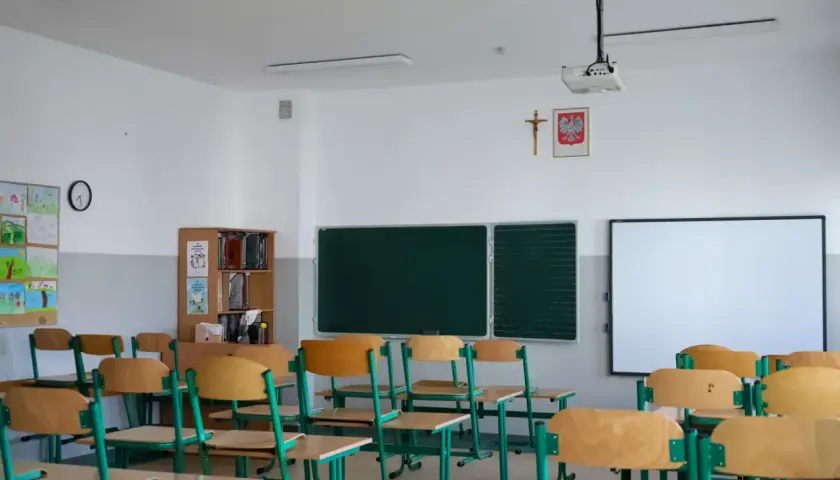 Pusta klasa szkolna z rzędami ławek, tablicą i projektorem.