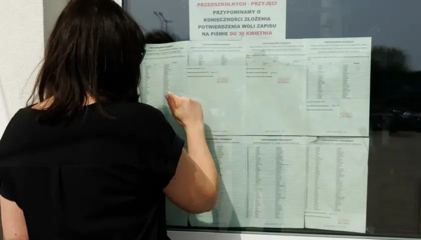 Kobieta w czarnej bluzce przegląda listę kandydatów do szkoły średniej.