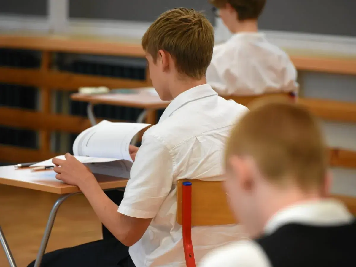 Uczeń w białej koszuli przegląda książkę przy ławce w klasie.