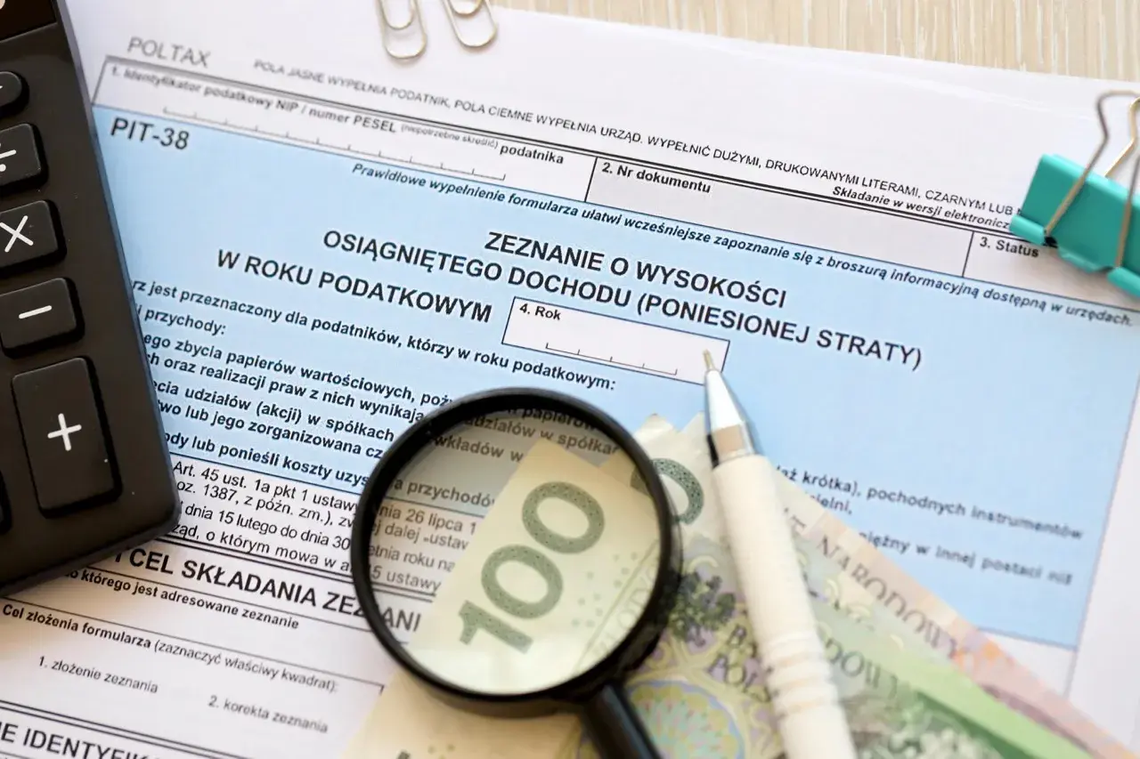Formularz PIT-38, kalkulator, lupa, długopis i banknot 100 zł.